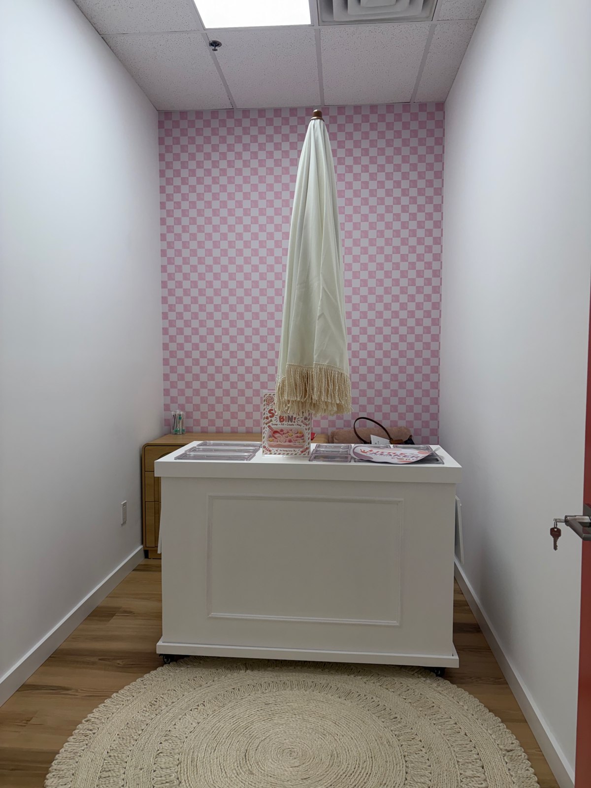 A cozy clinic nook with pink checkerboard wallpaper, a white cart, and a round woven rug