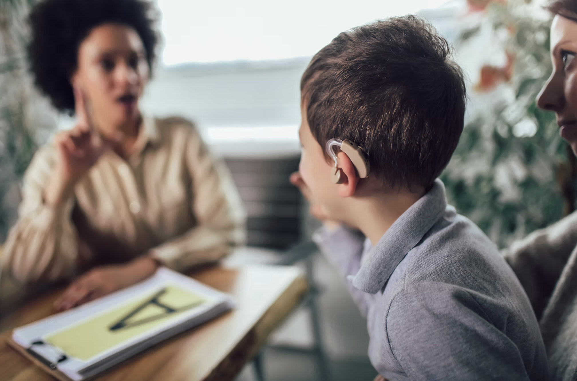A child wearing a hearing aid practicing communication with an adult and caregiver
