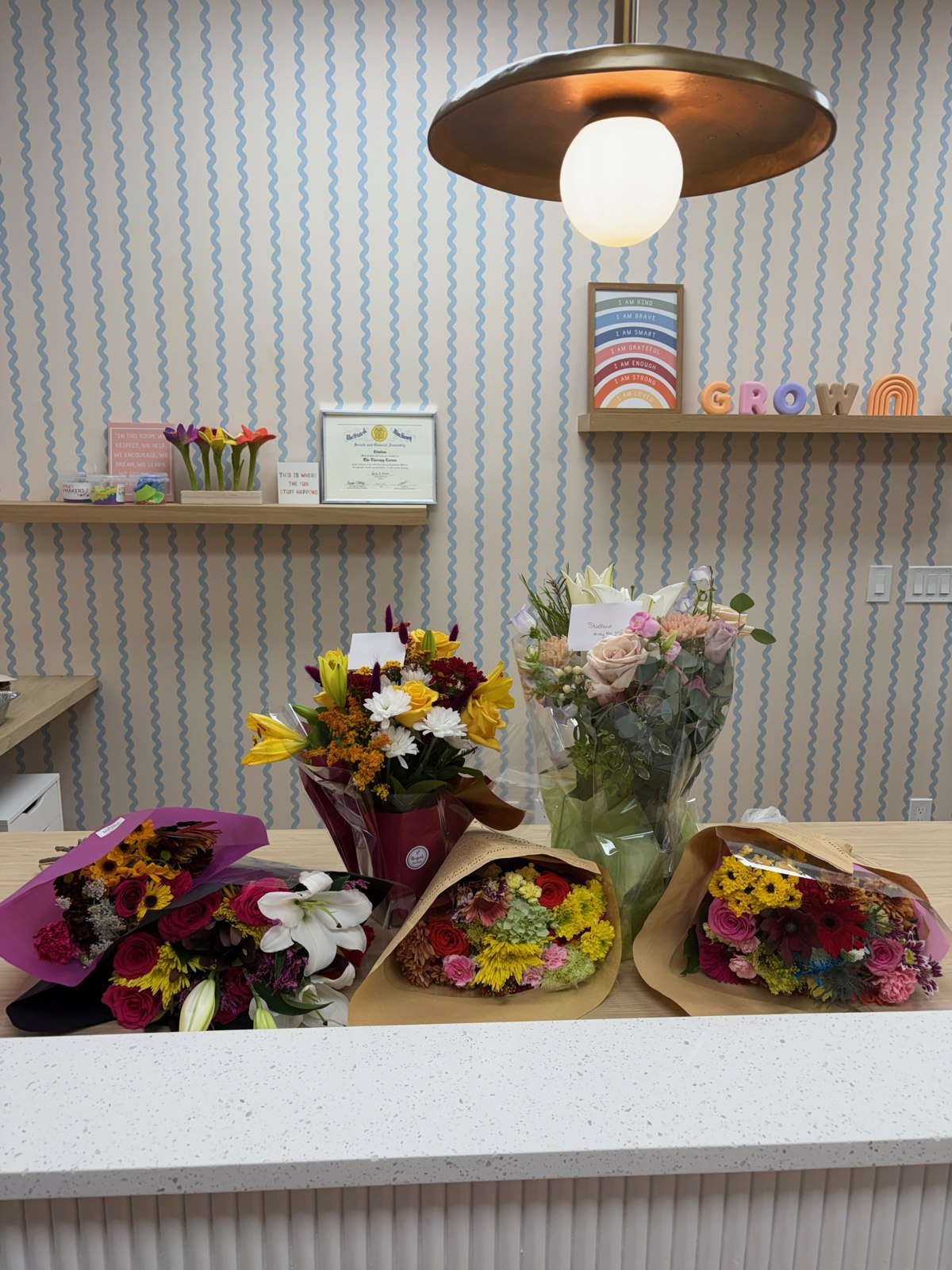 The Therapy Corner reception desk with blue wave wallpaper, wooden shelves, and fresh flowers